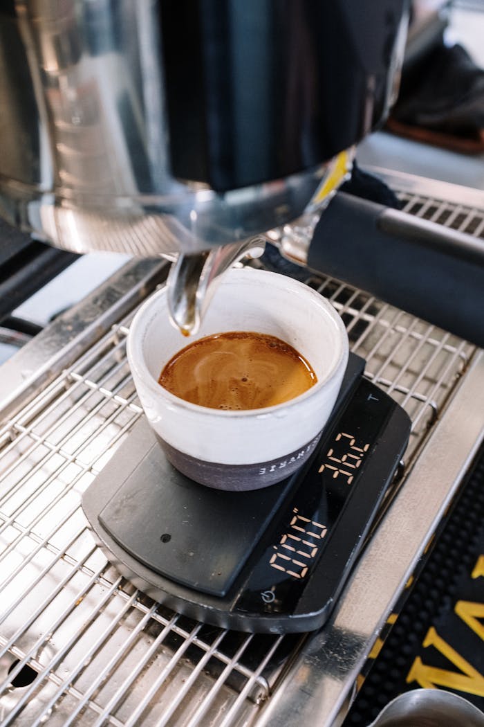 Espresso being brewed into a cup on a digital scale in a café setting.