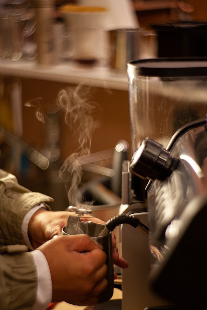 gallery-5 Close-up of barista's hands steaming milk with a coffee machine in a cafe.